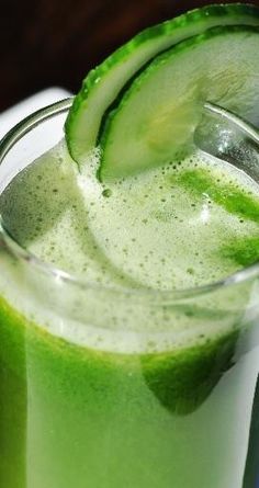 a green drink with a slice of cucumber on the rim