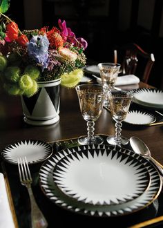 a black and white table setting with flowers in vases on the side, plates and silverware