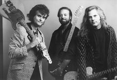 three men standing next to each other holding guitars