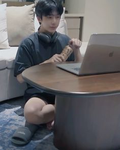 a young man sitting at a table with a laptop and cork in his hand while listening to headphones