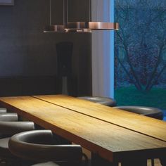 a long wooden table sitting in front of a window next to chairs and a lamp