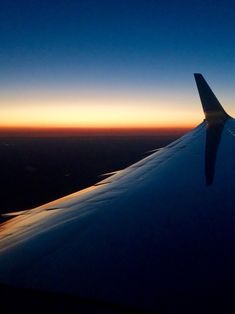 the wing of an airplane as it is flying in the sky at sunset or dawn