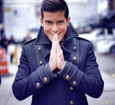 a man in a pea coat is smiling and making a hand gesture with his hands