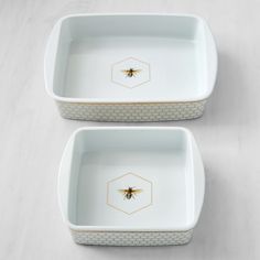 two white dishes with bees on them sitting on a counter top next to each other