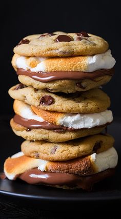 a stack of cookies with chocolate and marshmallows on top, sitting on a black plate