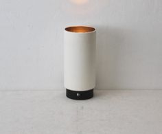 a white vase sitting on top of a table next to a light bulb and a wall