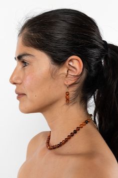 a woman wearing a necklace with beads on it's neck and earrings in front of her face