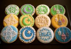 twelve decorated cookies in different colors on a black tray with white and blue icing