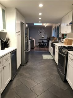 an empty kitchen with white cabinets and black floor tiles on the walls, along with stainless steel appliances