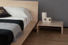 a bed sitting on top of a wooden floor next to a night stand with two candles