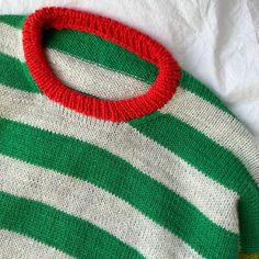 a green and white striped sweater with a red circle on the collar, sitting on a bed