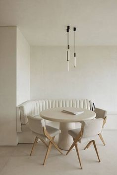 a round table with four chairs and a book on it next to a white couch