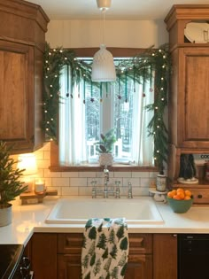 a kitchen decorated for christmas with garland and lights on the window sill, sink in foreground