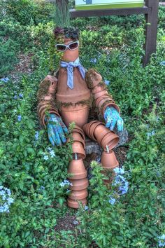 a scarecrow sitting in the middle of some flowers and plants with blue gloves on