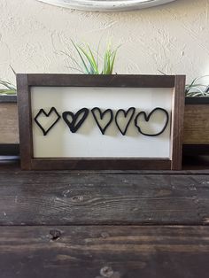 the word love spelled with hearts in a wooden frame on top of a table next to a potted plant