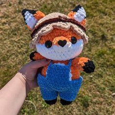 a hand holding a small crocheted stuffed animal in overalls and a hat