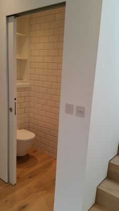 an open door leading to a bathroom with a toilet in the corner and shelves on the wall