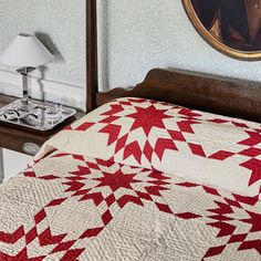 a bed with a red and white quilt on top of it next to a lamp