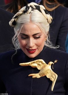 lady with white hair and braids holding a golden bird brooch in her hand