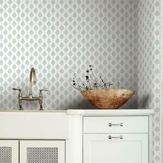 a sink with a bowl on top of it next to a cabinet and wall paper