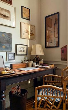 a desk with two chairs and pictures on the wall above it, along with a lamp