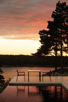 two chairs and a table are sitting on the edge of a pool as the sun sets