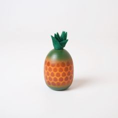 an orange and green ceramic vase with a leaf on it's top, against a white background