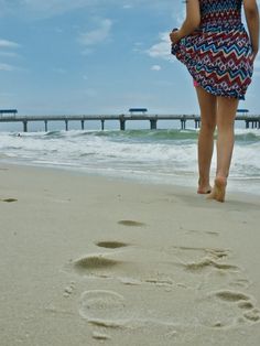 a woman walking on the beach with her foot prints in the sand next to the ocean