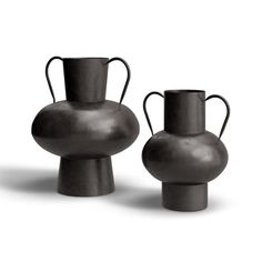 two black vases sitting next to each other on a white surface with no one around them