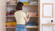 a woman standing in front of a closet filled with folded clothes and other clothing items