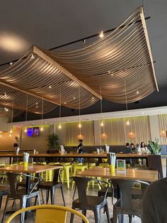 an empty restaurant with yellow chairs and wooden tables, along with people sitting at the bar