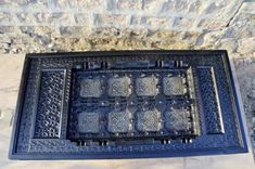 an ornately designed metal bench sitting in front of a stone wall