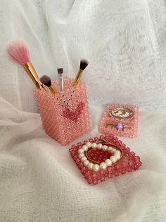 three makeup brushes in pink containers on a white sheet with beads and pearls around them