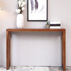 a wooden table topped with a white vase filled with flowers next to a framed photograph