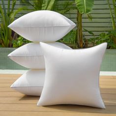 three white pillows stacked on top of each other in front of a swimming pool with palm trees