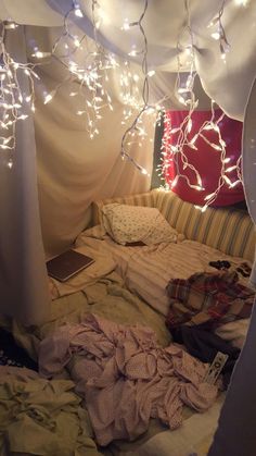 an unmade bed with white lights hanging from it's ceiling and pillows on the floor