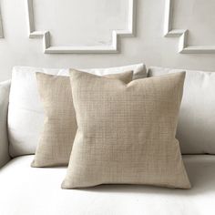 two pillows sitting on top of a white couch next to pictures hanging on the wall