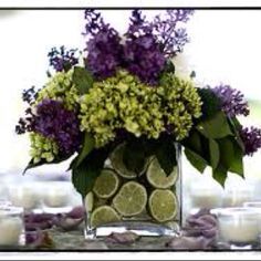 a vase filled with lots of purple flowers and lemon slices next to candles on a table