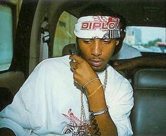 a man sitting in the back seat of a car talking on a cell phone while wearing a hip hop hat