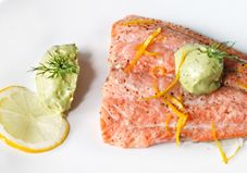 a piece of salmon with avocado and lemon on a white plate