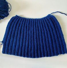 a blue knitted skirt next to a ball of yarn on a white table top