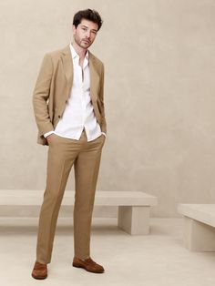 a man standing in front of a white bench wearing a tan suit and brown shoes