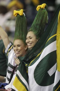 two girls with green hair and yellow bows are smiling while holding flags in their hands