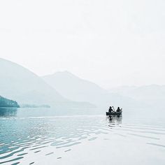 two people on a boat in the middle of a body of water with mountains in the background