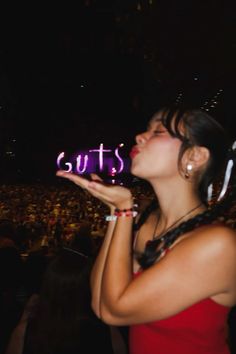 a woman in a red dress holding up a neon sign with the word guts on it