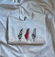 three embroidered t - shirts sitting on top of a white bed covered in sheets and pillows