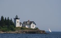 a lighthouse on an island with a sailboat in the water and trees around it