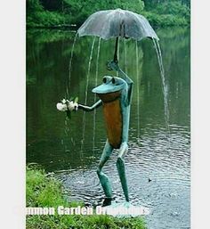 a frog statue holding an umbrella over its head while standing in front of a body of water