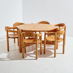 a wooden table and chairs are arranged in a circle on a white floor with shadows from the wall