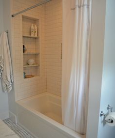 a bathroom with white tile walls and flooring, including a bathtub next to a shower curtain